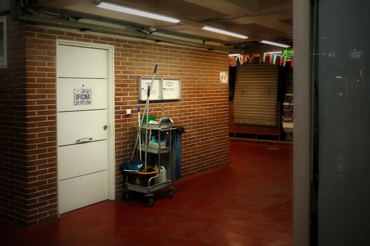 services-02 A brightly lit industrial hallway with a cleaning cart and supplies near an office door.