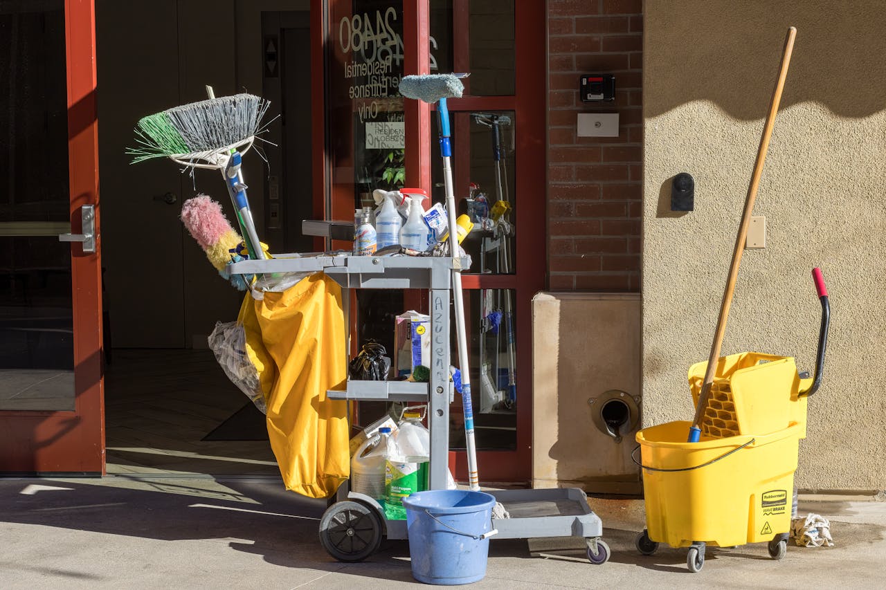 services-03 Cleaning supplies and tools outside a building entrance bathed in sunlight.