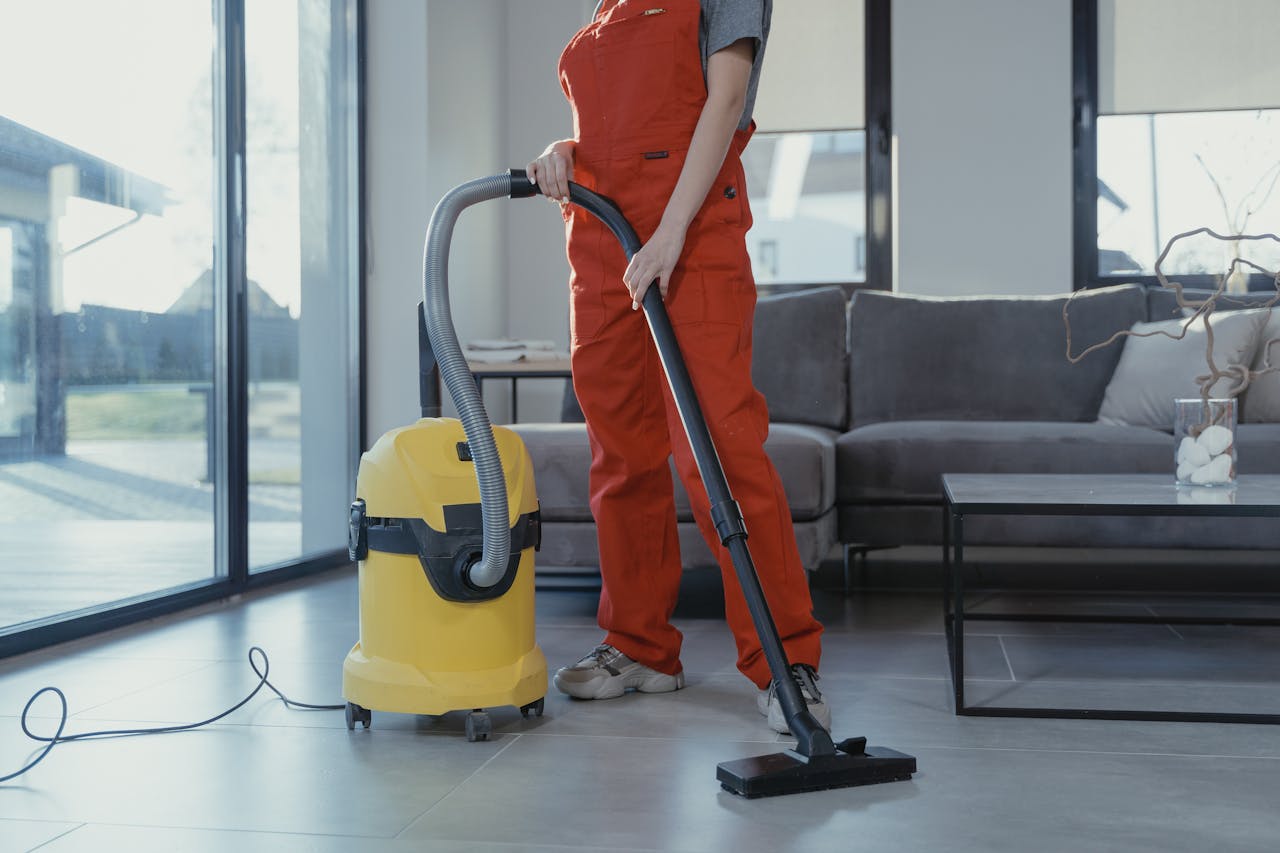 why-choose-us A professional cleaner in red coveralls vacuuming a modern living room with a yellow vacuum cleaner.