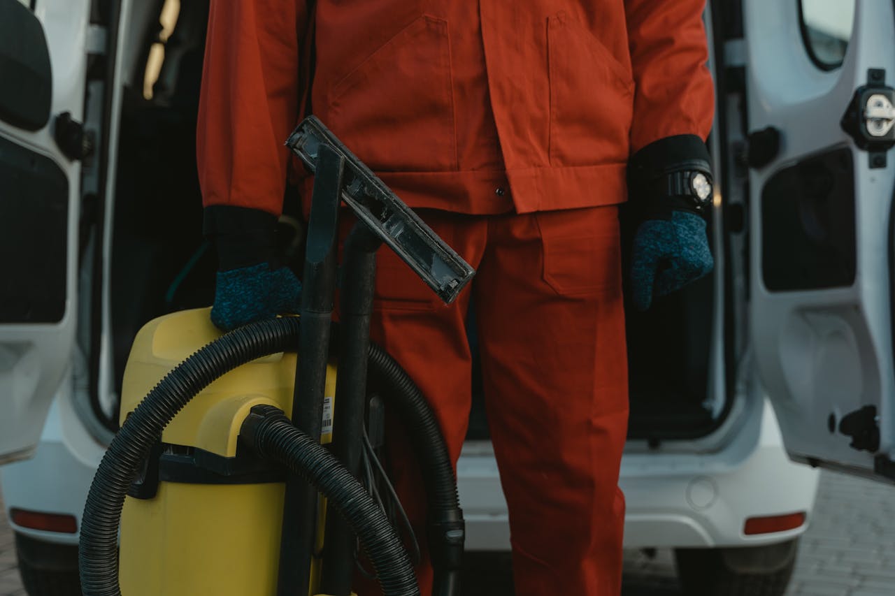 hero-img-02 A professional cleaner in a red uniform holding a vacuum near a van, ready for service.